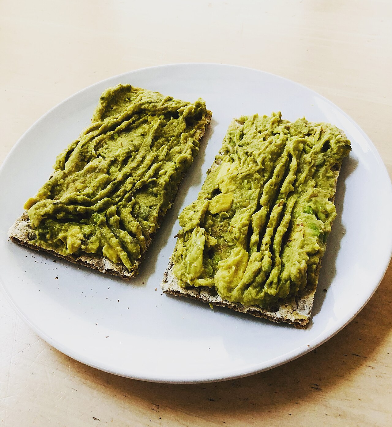 Two Wasa rye crispbreads spread with avocado hummus on a white plate
